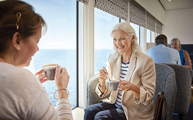Friends enjoying coffee in the Britannia Lounge on Spirit of Adventure