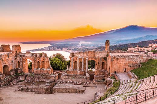 The sun sets behind Mount Etna with Taomina Greek Theatre in the foreground